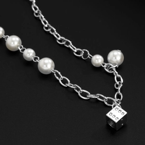 Detail of fashion splice necklace with metallic silver chain, pearls and dice pendant