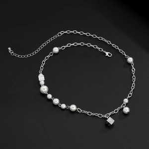 Detailed view of silver necklace with white pearls and metallic dice pendants on black