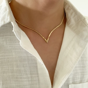 Detalle de colgante dorado en forma de V con cadena plana de serpiente en un modelo