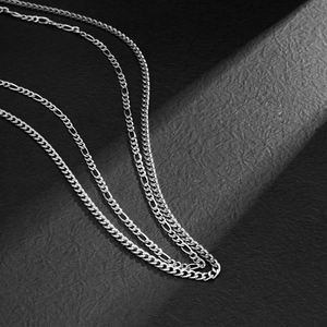 Detail of silver Figaro and Curb waist chain links on textured black background