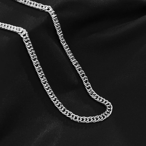 Detailed macro view of silver metallic curb link chain on elegant black silk background