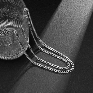 Detailed view of silver metal curb and figaro waist chains with polished texture
