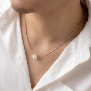 Detail einer Herren-Gold-Schlangenkette mit einer weißen Perle auf einem weißen Hemd