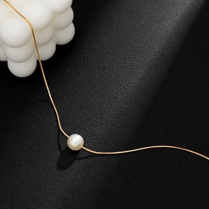 Detail einer minimalistischen goldenen Schlangenkette mit einer runden weißen Perle