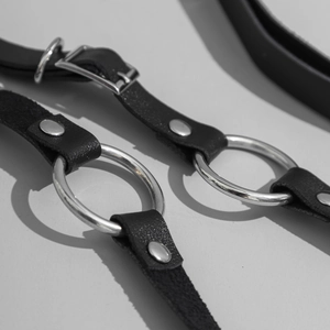 Detail of punk black leather body harness featuring metallic O-rings and silver rivets