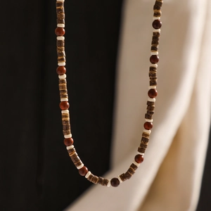 Close-up of bohemian beaded necklace with dark wood cylinders and red earthy round beads