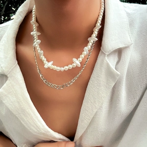 Close-up of layered baroque pearl necklace and silver metal link chain on white shirt