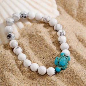 Macro view of white turquoise beaded bracelet with carved turtle charm on sandy beach