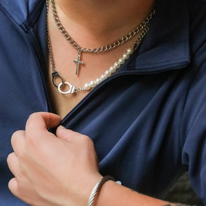 Close-up of pearl necklace with handcuffs clasp and cross pendant on male model