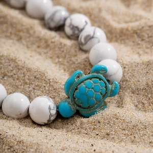 Macro shot of white turquoise beaded bracelet with green sea turtle charm on sand