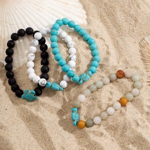 Close-up of beaded turtle bracelets with natural stones on white seashells and sand