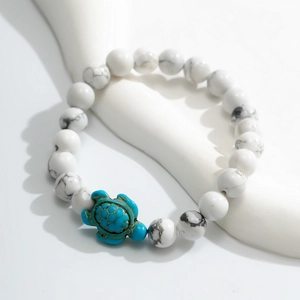 Detail of white marble beads and a turquoise turtle charm on a minimalist jewelry display