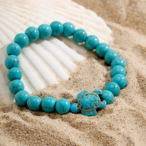 Detail of turquoise beaded bracelet with vintage turtle charm on a beach shell background