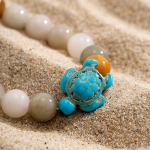 Detailed view of turquoise turtle charm and beaded bracelet on natural sand background
