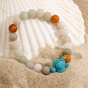 Men's beaded turtle bracelet with turquoise sea turtle charm on sandy beach background
