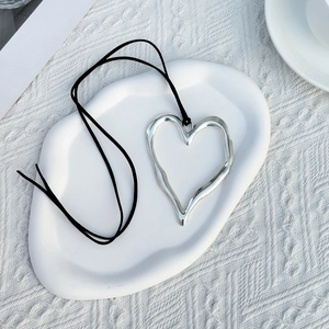 Collana minimalista con ciondolo a cuore e cordino nero su un elegante vassoio di ceramica