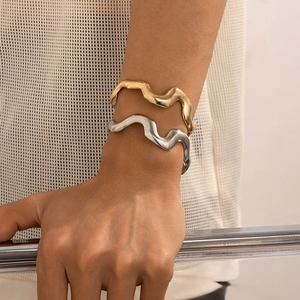 Close-up of wavy liquid metal cuffs in gold and silver finish on a model wrist