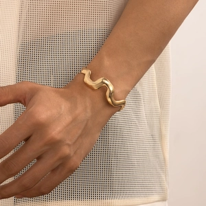 Detailed view of irregular wavy liquid metal bracelet in shiny gold finish on wrist