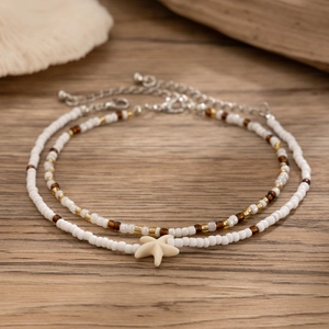 Detail of bohemian layered beaded anklets with white starfish charm on a wooden background