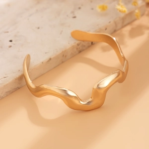 Macro detail of golden irregular wave bangle with matte texture on marble surface