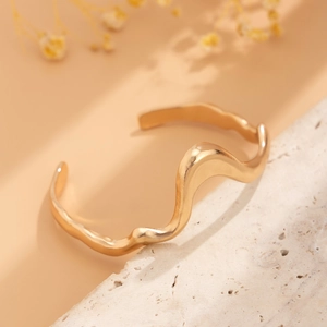 Detail view of wave-textured gold open bangle on decorative stone with floral background