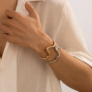 Detail of minimalist wavy open bangles in gold and silver finish on a male model