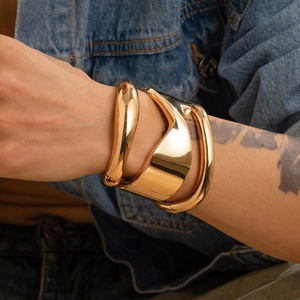 Dettaglio del bracciale rigido dorato con linee organiche irregolari su sfondo denim