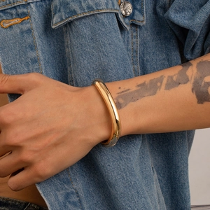 Dettaglio del bracciale rigido dorato minimalista indossato con giacca di jeans