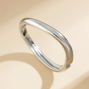 Bracciale ovale in metallo argentato lucido con chiusura a cerniera su sfondo beige
