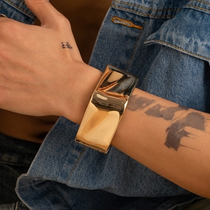 Dettaglio di un ampio bracciale dorato con texture irregolare su sfondo in denim blu scuro