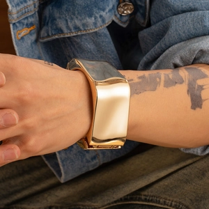 Bracciale a fascia in oro lucido al polso su sfondo di tessuto denim blu scuro