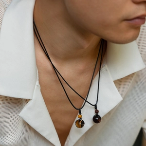 Detail of male model wearing layered turquoise bead pendants with black wax cord necklaces