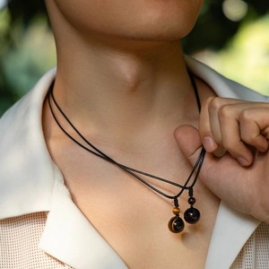 Detail of turquoise and tiger eye bead pendants on black leather cord worn by male model