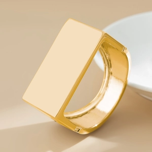 Dettaglio di un bracciale geometrico largo dorato con finitura a specchio su base beige