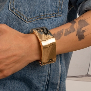 Dettaglio del bracciale rigido dorato irregolare da uomo con trama in metallo liquido lucido