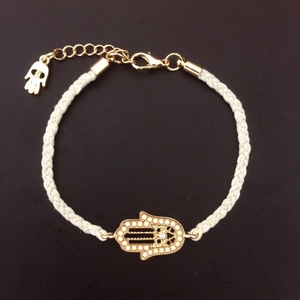 Handmade woven white cord bracelet with golden Hamsa Hand charm on dark background