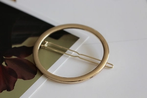 Detailed close-up of a minimalist circular gold-tone metal hair clip with a polished finish