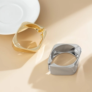 Bracciali quadrati lucidi in oro e argento con chiusura a molla su sfondo beige caldo