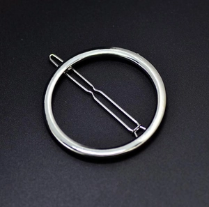 Close-up of a minimalist silver circular hair clip with a straight metal pin on a black background