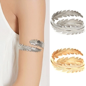 Macro detail of adjustable feather-shaped arm cuff in polished gold and silver finishes