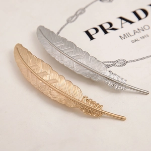 Macro view of gold and silver feather-shaped metal hair clips showing detailed texture