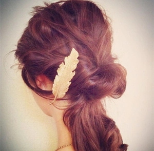 Detail of golden feather hair clip worn on elegant reddish-brown updo hairstyle