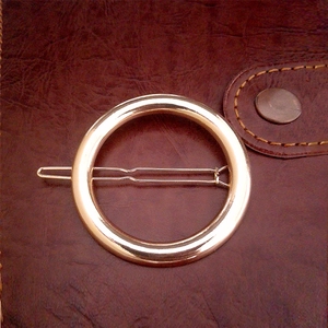Détail d'une pince à cheveux circulaire dorée minimaliste avec finition polie brillante