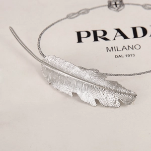Detailed view of silver feather hair clip with intricate metallic textures and curved design