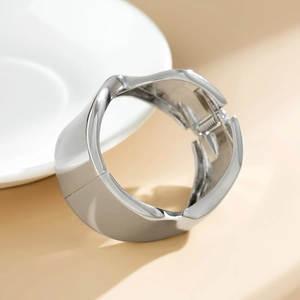 Dettaglio di bracciale largo argento lucido con bordi ondulati e chiusura a cerniera