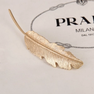 Macro shot of gold feather hair clip with detailed metallic texture on white background