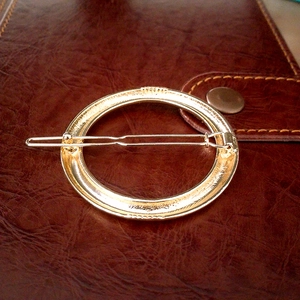 Pince à cheveux circulaire géométrique dorée sur fond de cuir texturé marron