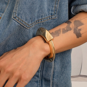 Dettaglio del bracciale industriale dorato con inserto testurizzato su braccio tatuato