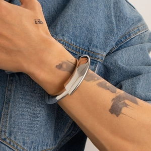 Bracciale rigido argento irregolare indossato su braccio tatuato con sfondo denim