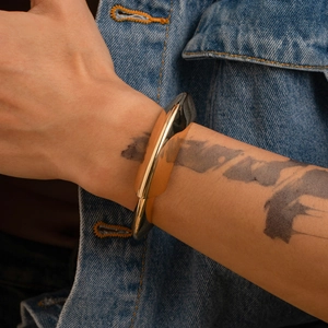Bracciale rigido scultoreo in metallo dorato con intarsio nero su braccio tatuato